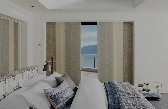 Panel glide blinds across a bedroom opening with a coastal view