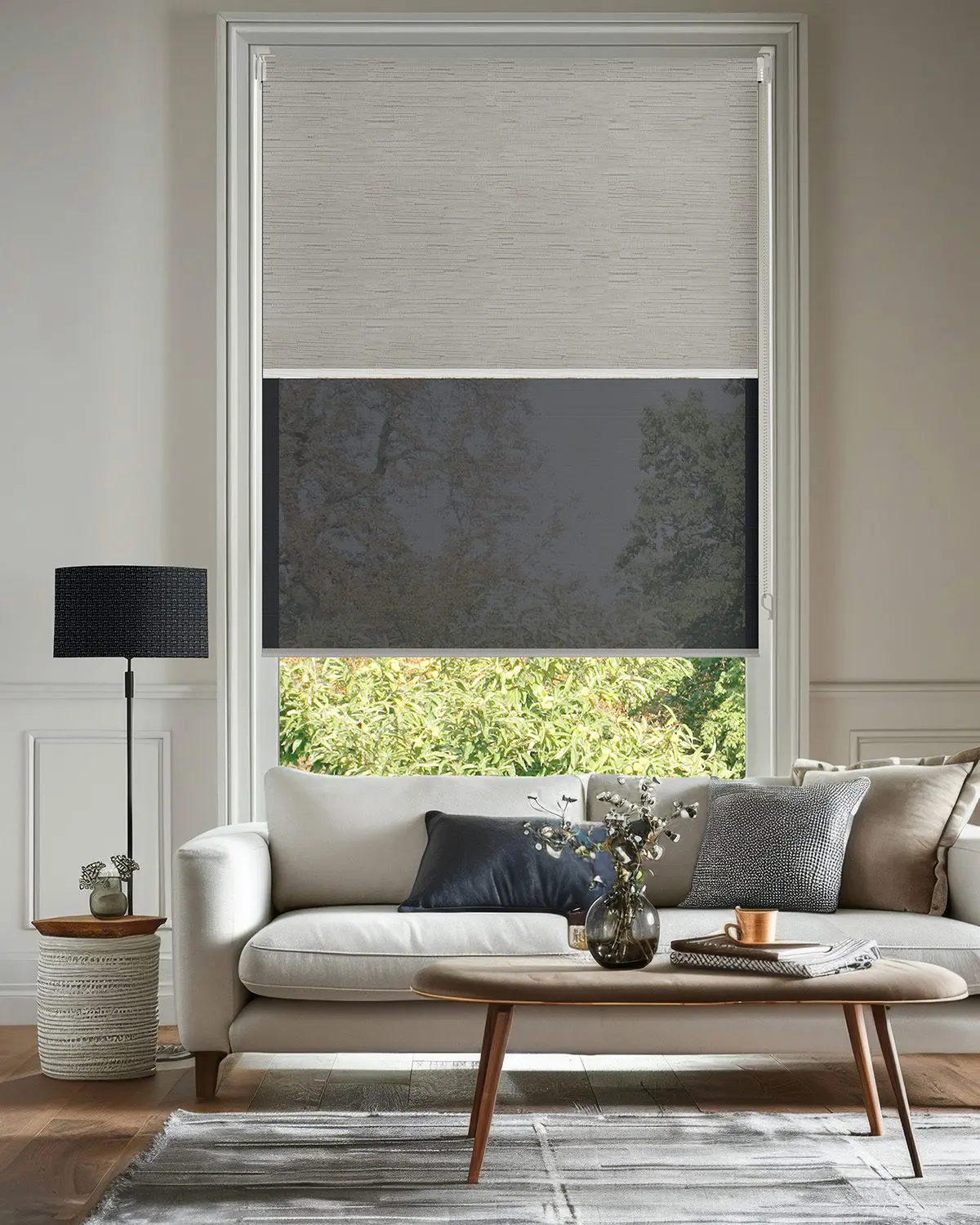 Double roller blinds combining light-filtering and darker privacy layers above a neutral living room sofa
