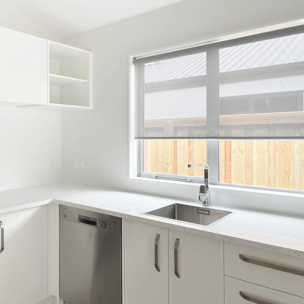 White sunscreen roller blind filtering daylight above a bright kitchen sink