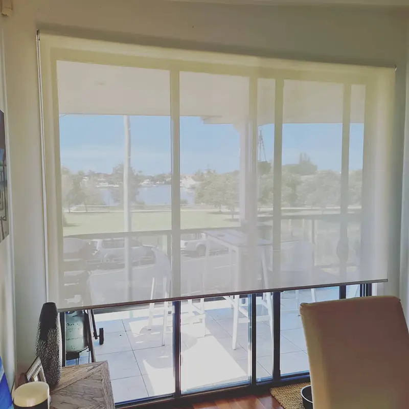 White sunscreen roller blind filtering daylight across a water-view dining room window